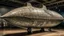 Placeholder: A gray military airship with tank planes designed in ancient Roman mosaics painted by Paul Klee