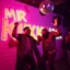 Placeholder: MR Kukrunk is Benny and DJ Roy in a disco, dancing, "Kukrunk" on sign wall, disco light, strobe, disco ball