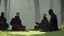 Placeholder: Black robed monks sitting around a fire in the forest