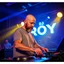 Placeholder: A dj on a night rave club standing mixing songs , he looks like Bryan Cranston kinda, bald with beard. strobes and blue yellow light, a big sign with "DJ ROY" in the background, this is a album cover for his dj roy assentials album.
