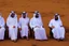 Placeholder: Four Arab sheikhs sitting in the desert wearing typical Arab dress, looking towards the four cardinal points. A talll fat european man in business suit wathhing them while thinking.