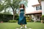 Placeholder: very beautiful lady with beautiful midi dark green-blue skirt and top with curvy hair sports shoes standing in a nice villa yard with trees flowers ,16 by 9