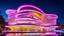 Placeholder: Enormous comical organic futuristic fantasy building at night, inspired by the fluidity of ocean waves: undulating, curved pink and yellow walls made of shimmering, innovative semi-transparent opalescent materials. The happy building has large, curved, intriguing rounded windows, iridescent curved balconies with big Disney sculptures. The building is surrounded by water and fountains. Snow-capped mountains on the horizon. Award-winning photograph, beautiful composition, joyful vibe, wonderful