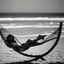 Placeholder: mujer sentada en una hamaca de madera en la playa, fotografía real, fotografía realizada con un cámara Fuji y objetivo de 35mm, fotografía en blanco y negro, tono años 60