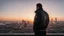 Placeholder: An Englishman in a bomber jacket standing to one side of a tall building looking across a city at sunset