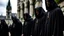 Placeholder: hooded monks in black robes in front of cathedral