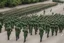 Placeholder: soldiers marching in formation; facing away from camera; military parade; tight formation; shoulder to shoulder; marching along a street; green uniforms; medals and insignia; long distance perspective; birds eye view; large parade;