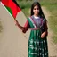 Placeholder: A very beautiful girl carrying a large Palestinian flag in her hands and waving it while wearing a keffiyeh and an embroidered Palestinian dress.