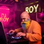 Placeholder: A DJ performing at dance club, his name DJ ROY and looks crazy, bald with crazy blue yellow beard. Neon lights and smog, DJ ROY SIGN ON WALL