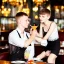 Placeholder: Russian guy boyish boylike short man's haircut boyish features in black girlish lacy cocktail dress as mother in restaurant