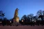 Placeholder: Park statue coming alive at twilight, stone becoming flesh gradually, pigeons unfazed, living monument