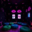 Placeholder: Fotografia di stanza oscuro weirdcore dai colori vivaci. Le pareti sono dipinte di nero chiaro con y stilizzate e dettagli come galli. Ci sono occhi rosa con finestrelle quadrate, che danno un senso distopico e molto surreale. Sul pavimento ci sono i rotonde e morbide, alcune verdi e altre blu, disposte in modo casuale. L'atmosfera generale sembra noiosa e onirica, con un contrasto tra elementi reali ed elementi dipinti