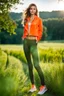 Placeholder: fullbody shot of young-beautiful-girl-with-a-perfect-face wearing sport pants and sport orange blouse and sport jacket and shoes standing in country side green field day lights