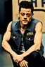 Placeholder: Polizeifoto Rami Malek mit Oberlippenbart in ärmelloser Denim Jacke und STP-T-Shirt, genervt in die Kamera starrend