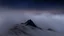 Placeholder: looking down at misty foreground and night sky background, no sun, single sharp narrow mountain peak coming through the mist in the center