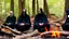 Placeholder: Black robed monks sitting around a fire in the forest