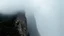 Placeholder: a scaling mountain cliff obscured by clouds and fog. the top 1/3 and bottom 1/3 of the image are fog, while the center is sheer cliff.