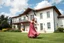 Placeholder: full body close up shot ,country side modern villa wide yard in front of villa ,a beautiful lady in nice long dress dancing in front of camera,flowers blue sky ,petty flophy clouds