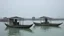 Placeholder: Dos pequeñs barcazas reposan sobre un mar tranquilo, en el fondo palafitos entre la niebla
