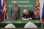 Placeholder: over the shoulder photo; politician signing a treaty; looking down; facing away, somber mood; in the background three banners, green banner, white banner, blue banner;