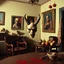 Placeholder: Flash photo of a room, 1980 horror movieshot, with chair, table, odd objects in background, ugly and scary mask, odd paintings hanging in the walls, rotten fruits, pair of glasses, horns, skin