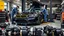 Placeholder: A car repair shop where two people in work clothes are repairing a black and yellow BMW M6 series with an eye-catching theme in a sophisticated and special repair shop where a collection of car engine parts is arranged on the floor at the bottom of the image.