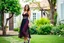 Placeholder: very beautiful lady with beautiful midi dark black-red lace skirt and lace top with curvy hair sports shoes standing in a nice villa yard with trees flowers ,16 by 9
