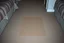 Placeholder: motel room floor, worn carpet with a faint rectangular discoloration where furniture used to be, uneven lighting, harsh flash photography, poorly framed, candid documentary photo, no clear subject