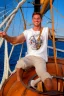 Placeholder: a cheerful sailor sitting on rum barrels aboard a sailing ship at sea, with the ship's steering wheel in the background