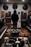 Placeholder: music producer wearing a hood looking at 3 vinyl records in the background of his modern studio. the picture is taken from above and behind. you can only see the back of the guy. you can see more of the modern room and the electric guitar there. you cant see the face of the person. make the guitar more present