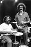 Placeholder: Frank zappa playing bongos next to a very fat black man