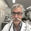 Placeholder: selfie of a white doctor in the break room; gray hair, mustache; nerdy glasses,