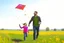 Placeholder: a father, a girl and a boy with a kite flying in the sky on the green field with flowers in sunshine