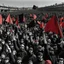 Placeholder: plano frontal de una multitud marchando en un reclamo popular, ondean banderas rojas y banderas negras, hay dolor pero un fuerte sentido de lucha en la multitud, atmosfera epica, victoria del pueblo, reivindicación de derechos y justicia, paleta roja, negra y blanca