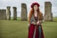 Placeholder: A tall slim red-headed young woman, dressed like a gipsy, standing in front of Stonehenge