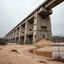 Placeholder: Fotografia di un grande ponte moderno brutalista, che sembra un tugurio, parzialmente sommerso. La struttura è erosa e inglobata dal paesaggio naturale, come se il tempo o l'ambiente avessero iniziato a "riassorbirla". No. L'atmosfera è desolata e surreale, con un ambiente circostante spoglio e sabbioso hasselblad h6d400c --ar 85:128 --v 6.0