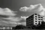 Placeholder: landscape ,minimal ,Photo with an old analog camera. Black and white. Part of a strange dream. white clouds wide plain The big building between them. like pink floyd pigs land scape from a weird dream captured with the first model of dreamrecorder by gnom industries inc