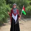 Placeholder: A very beautiful girl carrying a large Palestinian flag in her hands and waving it while wearing a keffiyeh and an embroidered Palestinian dress.