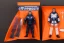 Placeholder: Mike pence G.i. Joe toy doll Space force uniform With accesories inside a blister packaging hanging on a Wall rack in toystore, fluorescent orange, toy guns, wide angle shot whole body, black moonboots, fullsize