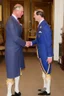 Placeholder: The Prince of Wales in traditional dress shakes hands with a guest in a blue suit, drawing room of St James's Palace, during a reception