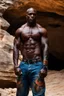 Placeholder: Alimi Ballard as very muscular male. bald with tribal tattoos wearing jeans and a teeshirt outside a cave