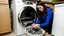 Placeholder: very confused young woman places a few metal spoons into her household dryer