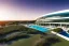 Placeholder: Sunset algarve in quinta do lago, one straight line building of 250 meters long modern luxury architecture with pool on rooftop, with green roofs and sun loungers next to pool, overlooking a tennis sport facility surrounded by pine trees, on a slope with pinus pinea, a wrap around road for low speed cars