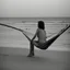 Placeholder: mujer sentada en una hamaca de madera en la playa, fotografía real, fotografía realizada con un cámara Fuji y objetivo de 35mm, fotografía en blanco y negro, tono años 60