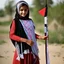 Placeholder: A very beautiful girl carrying a large Palestinian flag in her hands and waving it while wearing a keffiyeh and an embroidered Palestinian dress.