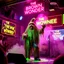 Placeholder: An "BIG POOP" performing at dance club, his name is "BIG POOP" and looks crazy, and green slime on stage, Neon lights and smog, "DAS BRAUNE WUNDER" SIGN ON WALL