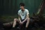 Placeholder: thin 17 year old male with short dark hair and blue eyes wearing a ripped and dirty white teeshirt sitting on a log , photorealistic, 4k, dark fantasy