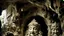 Placeholder: A large stone cave carved into a rock formation and abundantly carved in a baroque or rococo style, with a human face with an elaborate headdress or crown, surrounded by intricate decorative elements, human and organic figures, mythological animals, leaves and plants. The face appears to be that of an older man with a serious expression.