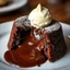 Placeholder: A decadent Molten Lava Cake, oozing with hot molten chocolate from its cracked center, elegantly presented on a plate with a dollop of creamy ice cream perched on top. This sumptuous dessert is depicted in a photograph, capturing the richness of its textures and colors. The luscious chocolate appears almost liquid, while the cake's exterior glistens with a hint of golden crust. The ice cream melts slightly, creating a tantalizing contrast of temperatures. The image exudes a sense of indulgence a