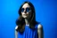 Placeholder: advertising photography, plain blue background, woman in blue dress, brunette, round sunglasses, real photography, 16K, shot with Leica camera, 35 mm lens, indirect lighting,